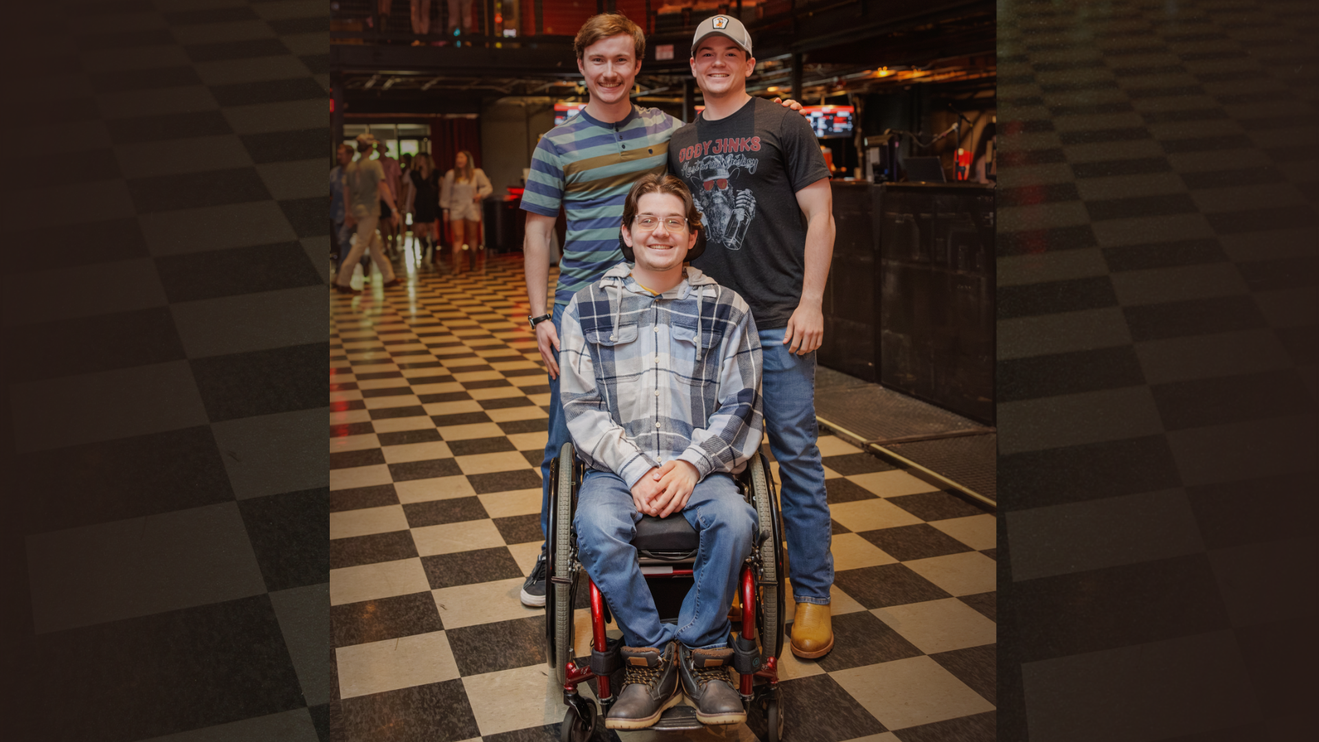 Two men standing and one man in a wheelchair smiling with a checkerboard tile floor