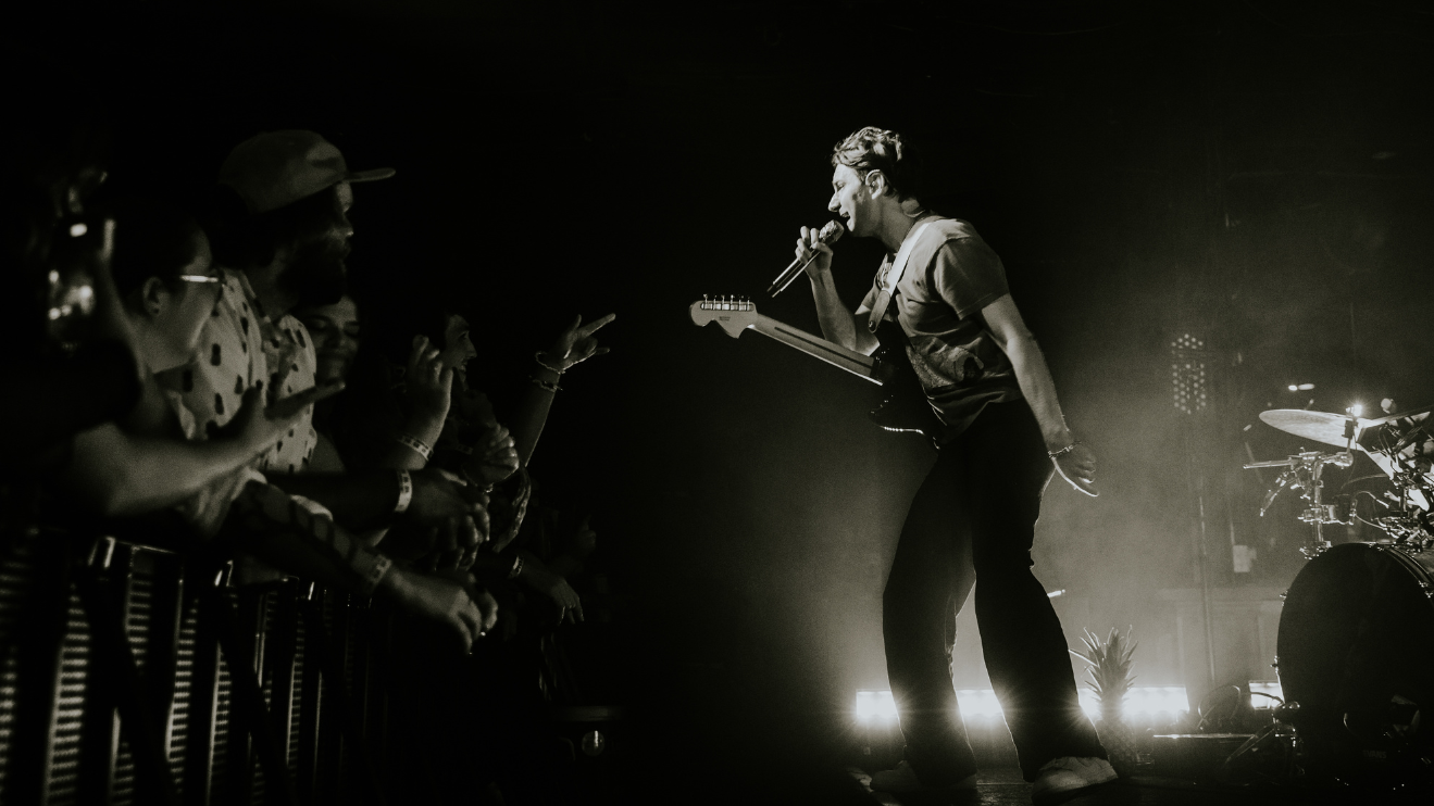 Photo of Glass Animals on stage performing at The Underground with people singing along the barricade. 